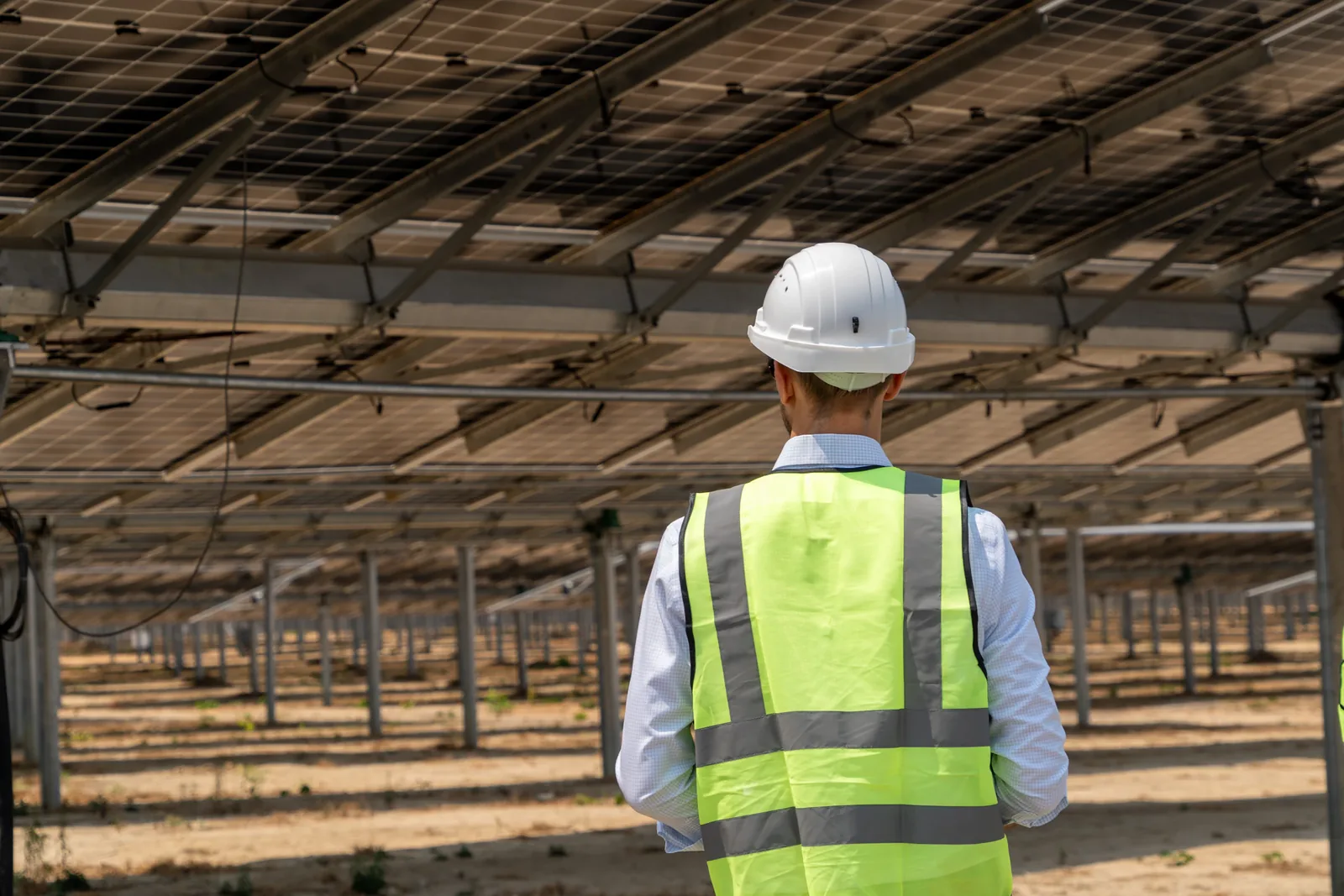 Engineer in a white safety helmet and reflective vest inspecting a solar panel site.